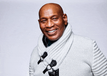 a smiling bald man wearing a white sweater with black buttons