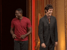 a man in a suit and a man in a red shirt are laughing together