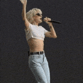 a woman wearing sunglasses and a white shirt is holding a microphone