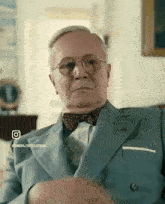 a man in a suit and bow tie is sitting on a couch