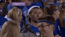 a man wearing a headband that says kansas state stands in a crowd of people