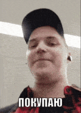 a man wearing a black hat and a red plaid shirt has the word покупаю on his face