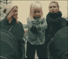 a little girl looking at a cell phone while standing next to two women