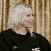 a woman with blonde hair is wearing a black sweater and smiling .