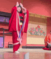 a woman in a red kimono is dancing in front of a painting of flowers