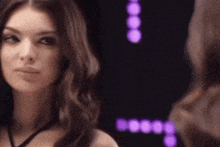 a woman is looking at herself in a mirror with purple lights in the background .