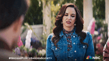 a woman in a denim jacket is talking to a man in a garden with the hashtag #grossepointegardensociety