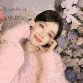 a woman in a pink sweater stands in front of a wall of flowers with the date 2022 on it