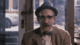 an older man wearing a hat and bow tie looks at the camera