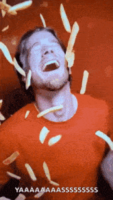 a man in a red shirt is laughing while french fries are falling around him .