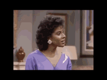 a woman in a purple dress and earrings is standing in a living room .