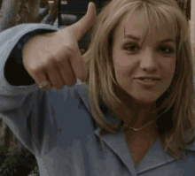 a woman in a blue shirt gives a thumbs up sign