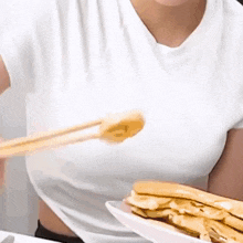a woman in a white shirt is eating a sandwich with chopsticks