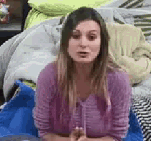 a woman in a pink shirt is sitting on a bed with a blanket .