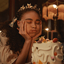 a young girl wearing a tiara blows out a candle on a cake