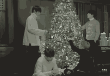 three men decorating a christmas tree with one wearing a sweater that says all the world 's magic