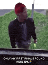 a man wearing a red hat and a black jacket is standing in front of a grassy hill .