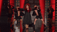a drag queen in a red dress is surrounded by men in black