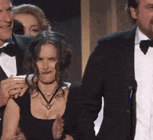 a man in a tuxedo stands next to a woman in a black dress making a face