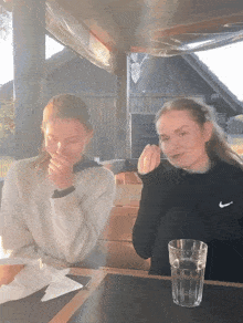 two girls sitting at a table with one wearing a nike sweater
