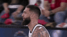 a man with a beard and a tattoo on his arm looks to the side during a basketball game