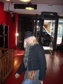a woman wearing a black jacket and a hat is standing in a room