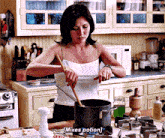a woman in a white tank top is stirring a pot with a wooden spoon .