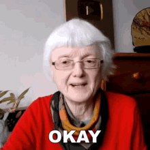 an older woman wearing glasses and a red shirt says okay