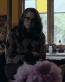 a woman wearing glasses and a plaid sweater sits at a table