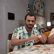 a man in a green and white striped shirt is sitting at a table with his hands in the air .