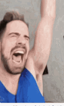 a man with a beard and a blue shirt is laughing with his arm in the air .