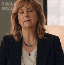 a woman wearing a black jacket and a necklace with the words small achievable goals on the bottom right
