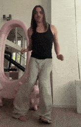 a man with long hair and a mustache is dancing in front of a pink sculpture