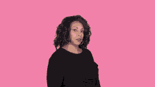 a woman in a black dress is pointing her finger at the camera on a pink background