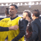 a group of soccer players are standing next to each other . one of the players is wearing a yellow kappa jersey .