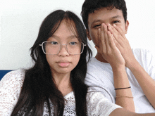 a boy and a girl with glasses covering their faces with their hands