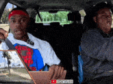 two men are sitting in a car and one is wearing a headband that says nike on it