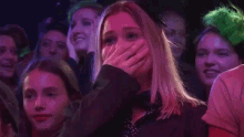 a woman is covering her face with her hand while sitting in a crowd of people .