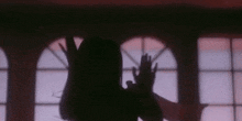a shadow of a woman standing in front of a window with her hands up .