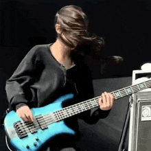 a woman is playing a blue bass guitar in front of a black background .