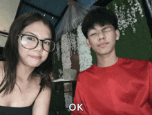 a boy and a girl are posing for a picture and the boy is wearing a red shirt that says ok on it
