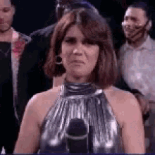 a woman in a silver dress is standing in front of a microphone in a crowd .