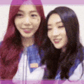 two women are standing next to each other and smiling . one of the women has red hair and the other has black hair .