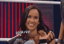 a woman in a wrestling ring is smiling and holding a wrestling championship belt .