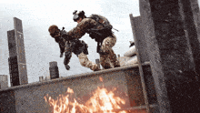 a soldier helps another soldier over a fire while another soldier looks on