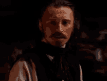 a man with a beard and mustache is wearing a black vest and a white shirt .