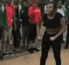 a woman in a black crop top and black pants is dancing in front of a crowd of people .