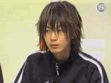 a young man with long hair is wearing a black jacket with white stripes on the sleeves ..