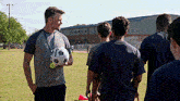 a man is holding a soccer ball with a medal around his neck while talking to a group of boys .