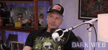 a man wearing a hat and a t-shirt is sitting in front of a microphone with the words dark web on the bottom